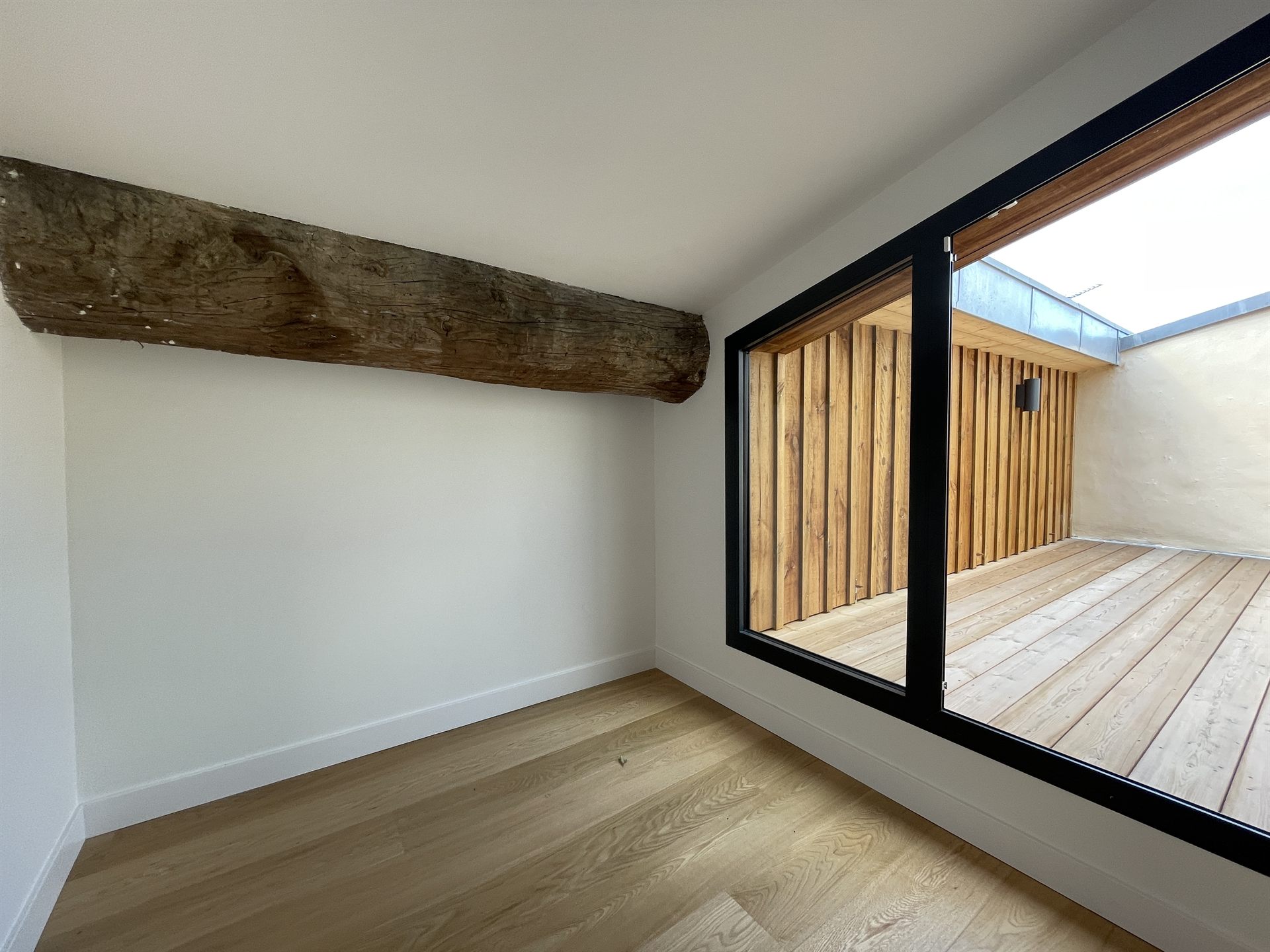 Chambre avec poutre ancienne et baie vitrée ouvrant sur la terrasse